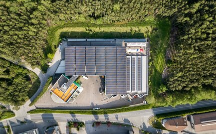 An overhead shot of the Zingerle Group production facility showing solar panels on the roof. The building is surrounded by trees.