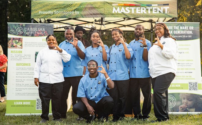 A group of catering chefs stand in front of a custom 10x10 canopy tent. 