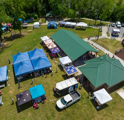 An aerial shot of many canopy tents set up on a waterfront park for an event.