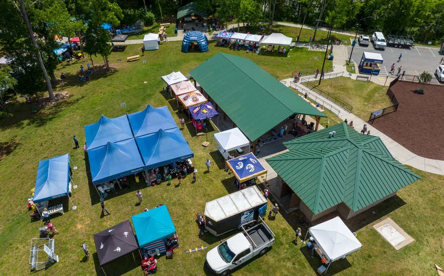 An aerial shot of many canopy tents set up on a waterfront park for an event.