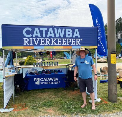 A man standing in front of a printed flat roof canopy tent at an outdoor environmental festival. 