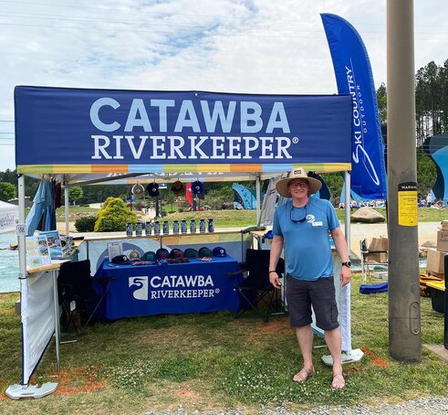 A man standing in front of a printed flat roof canopy tent at an outdoor environmental festival. 