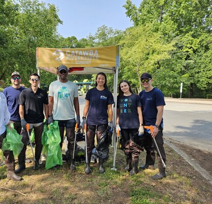 Participants of an outdoor cleanup stand in front of a 5x5 custom canopy tent. 