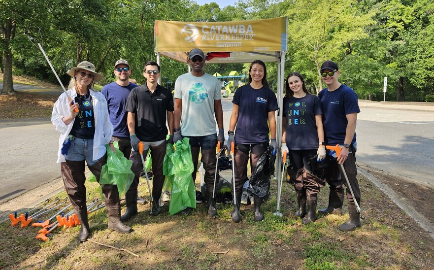 Participants of an outdoor cleanup stand in front of a 5x5 custom canopy tent. 