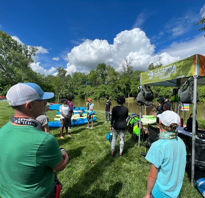 A custom 5x5 tent created for Catawba Riverkeeper sits along the river while volunteers stand nearby. 