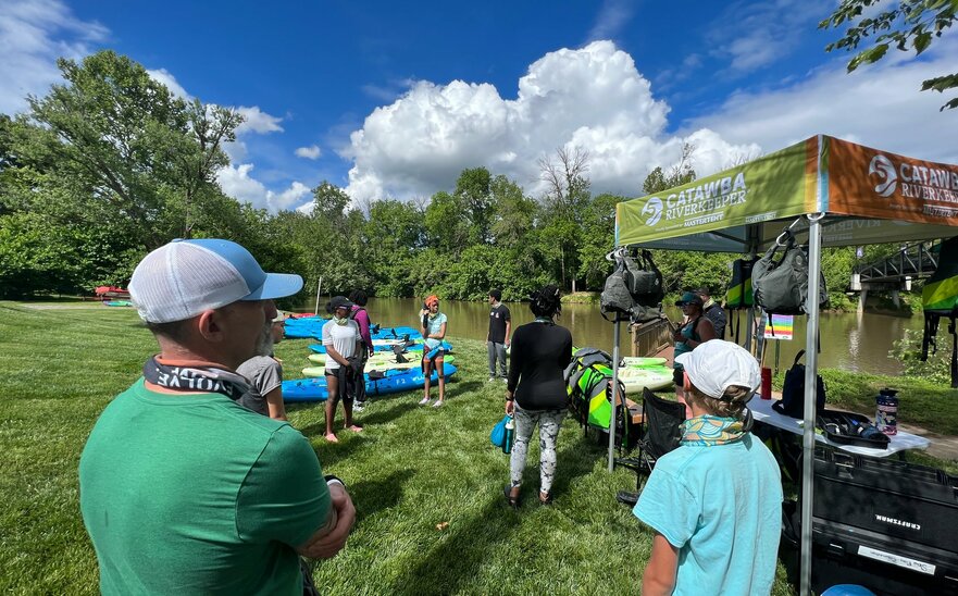 A custom 5x5 tent created for Catawba Riverkeeper sits along the river while volunteers stand nearby. 