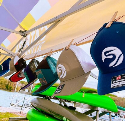 A row of Catawba Riverkeeper hats hang off of a Mastertent canopy tent valance. The tent is custom printed with the organization's branding and lettering.