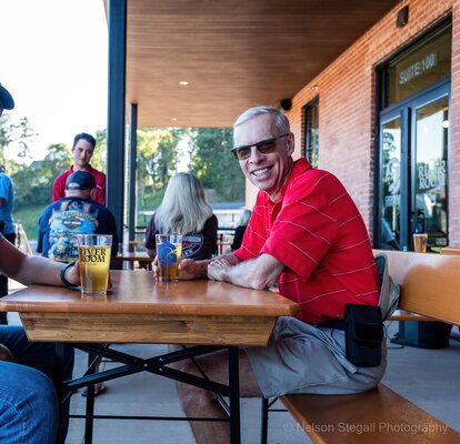 Visitors sit on the patio of The River Room on RUKU1952 folding wood tables and benches. 