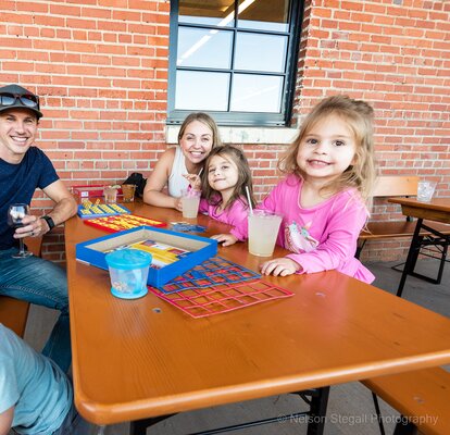 A family sits on the patio of The River Room on RUKU1952 wood folding tables and benches. 