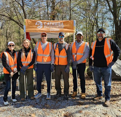 Participants of an outdoor cleanup stand in front of a 5x5 custom canopy tent. 