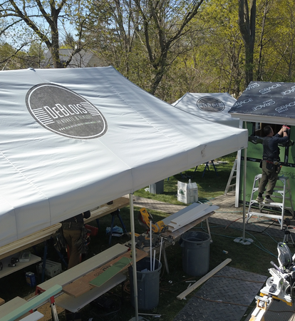 The photo shows three Mastertent folding gazebos with the DeBlois Renovate & Remodel logo. A craftsman stands on a ladder and carries out work on a house.