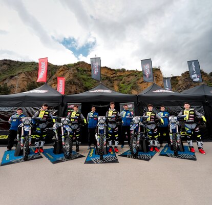 Nella foto ci sono tre gazebo pieghevoli neri con bandiere. I gazebo sono personalizzati con il logo del team di motociclisti. I motociclisti e le loro moto stanndo davanti ai gazebo.