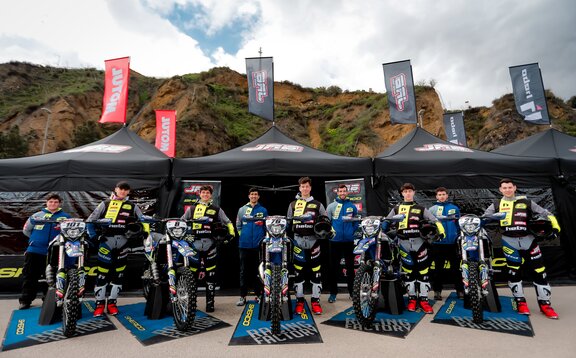 The picture shows three black folding gazebos with flags. The gazebos are printed with the logo of the motorbike team. The team is standing in front of the tents.