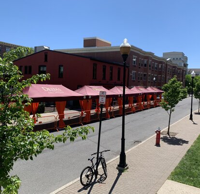 A row of Mastertent Series 1 20x10 canopy tents arranged in a multi-tent system for outdoor dining. Bordeaux roof and orange corner curtains branded for Delta's Restaurant.