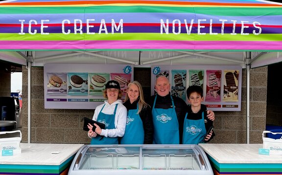 A bright, colorful printed tent over an ice cream serving station. Roonie's Ice Cream owners and family underneath.