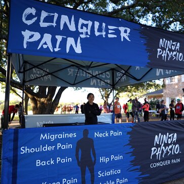 A Mastertent Square 10x10 canopy tent printed in black and blue as an information booth for Ninja Physio chiropractic care. 