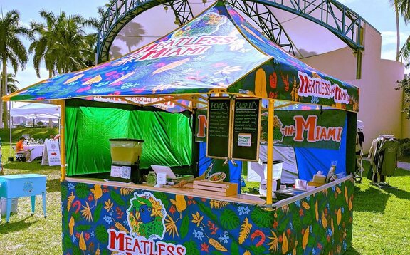 A Mastertent folding gazebo printed with colourful patterns with an awning and with a counter to serve food.