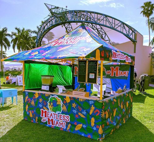 A Mastertent canopy tent printed with bright colorful patterns with counters to serve food.