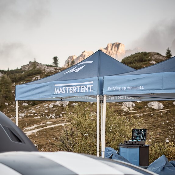 Blue printed canopy tents with Mastertent logos set up with mountains in the background.