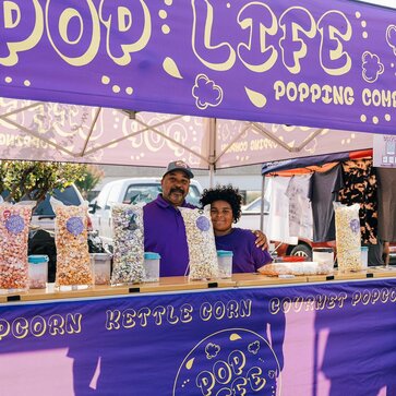 A purple 10x10ft printed canopy tent with counters to sell popcorn.