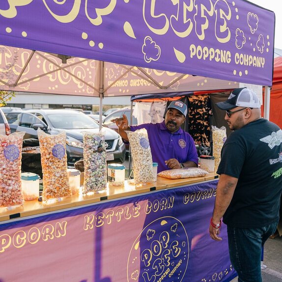 A purple 10x10ft printed canopy tent with counters to sell popcorn.