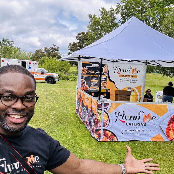 A man standing in front of his Mastertent printed vending canopy tent with awning on a grass field.