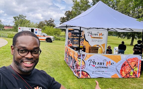 A man standing in front of his Mastertent printed vending canopy tent with awning on a grass field.