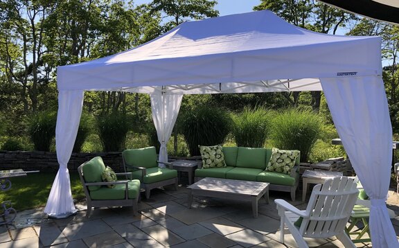 A 15x10 white canopy tent with a white frame creates shade above a backyard patio. 