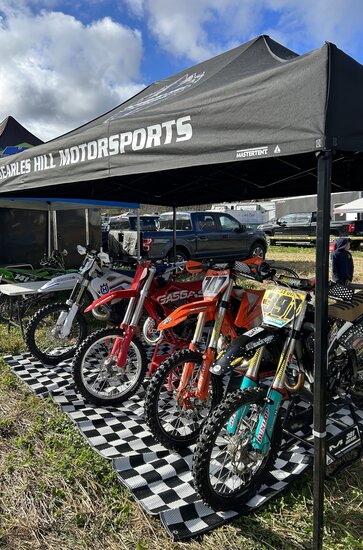 A 15x10 custom motorsports tent with a black roof covers dirt bikes prior to a race. 
