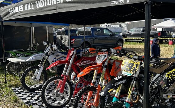 A 15x10 custom motorsports tent with a black roof covers dirt bikes prior to a race. 