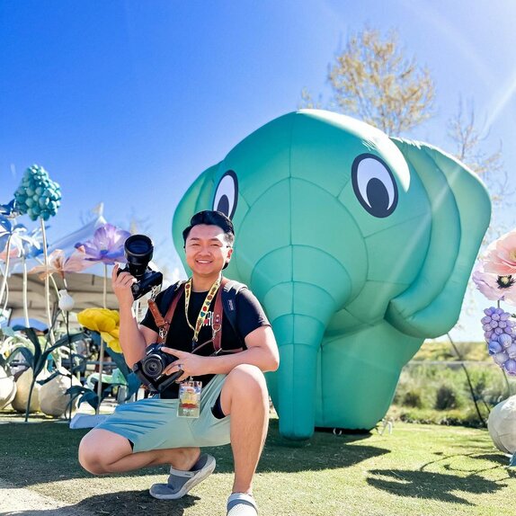 A photographer posing in front of a green custom inflatable elephant at Sabaidee Fest. | © @chueleephotodesign