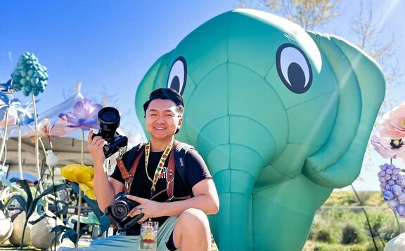 A photographer posing in front of a green custom inflatable elephant at Sabaidee Fest. | © @chueleephotodesign