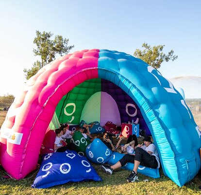 A multi-color dome inflatable advertising structure set up in a park for an event.