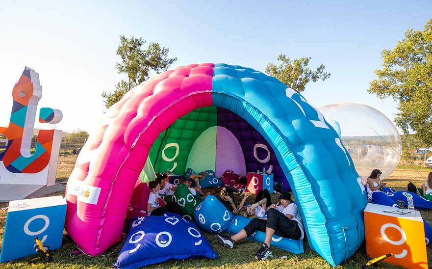 A multi-color dome inflatable advertising structure set up in a park for an event.