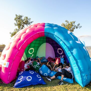 A multi-color dome inflatable advertising structure set up in a park for an event.