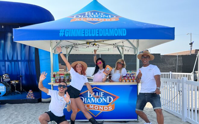 Crowd pose for picture on the sand under Blue Diamond branded Mastertent square pavilion.