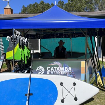 Catawba Riverkeeper pavilion set up with man in shade behind paddleboard.