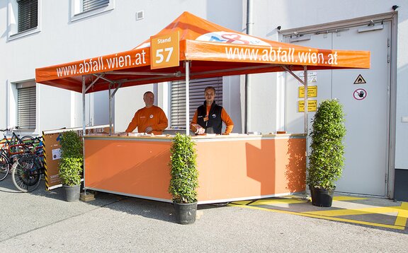 Orange hexagonal pavilion with smiling attendants. 