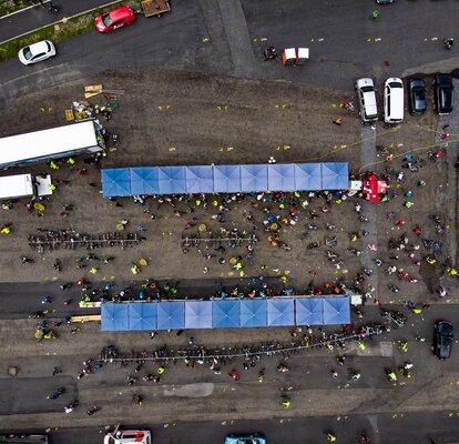 Two lines of nine square, blue Mastertent canopy tents on asphalt seen from above with people and cars crowded around.