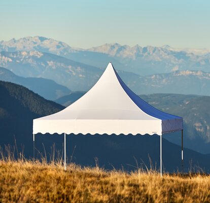 White tent with high peak and scalloped valances in a field with mountains in background