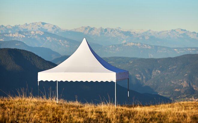 White tent with high peak and scalloped valances in a field with mountains in background