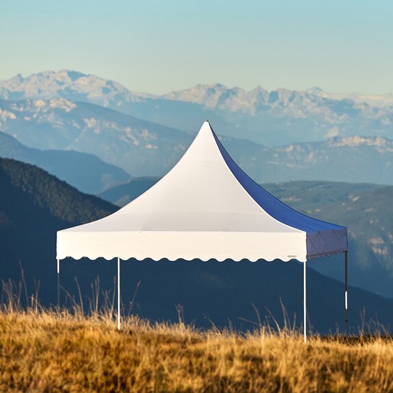 White tent with high peak and scalloped valances in a field with mountains in background