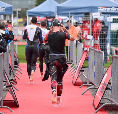 Three men in swim body suits running away from camera in triathlon with fans crowded on either side