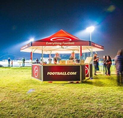 Red pavilion for football club on green football field with blurred people in crowd at night