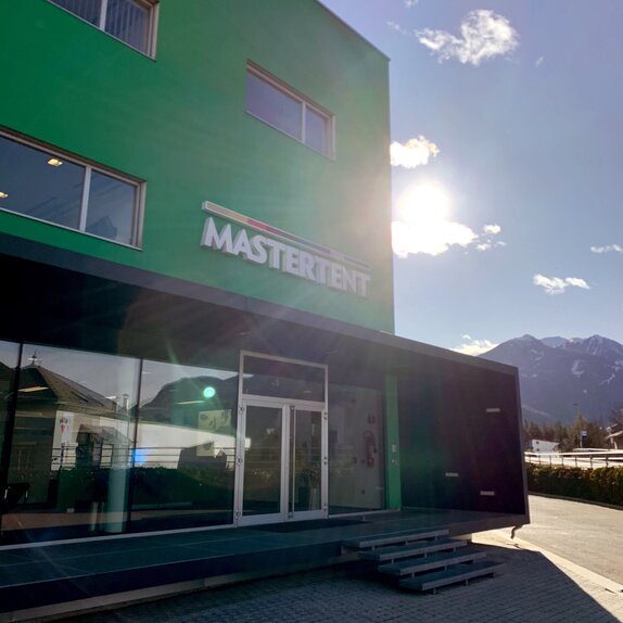 A modern, three story, green building with large windows on the bottom floor on a bright, sunny day