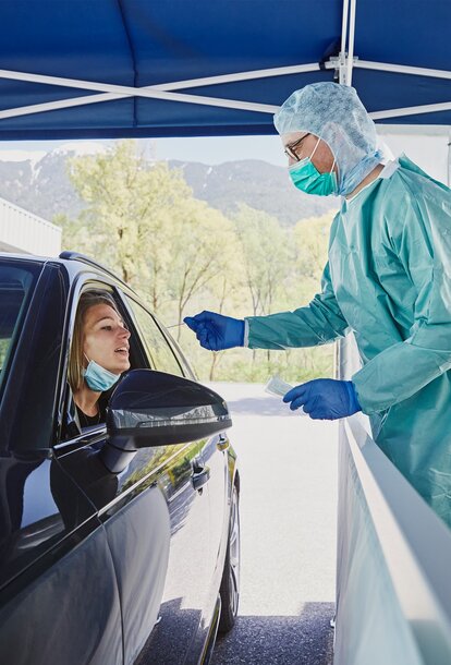 Der Mitarbeiter vom Krankenhaus macht in der Drive-In Teststation gerade einen Abstrich bei der Frau im Auto.