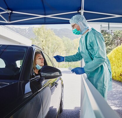 Der Mitarbeiter vom Krankenhaus macht in der Drive-In Teststation gerade einen Abstrich bei der Frau im Auto.