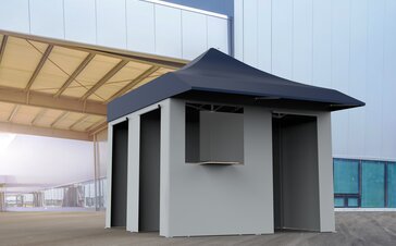 The vaccination tent is standing in front of a building. It has a blue roof and grey sidewalls.