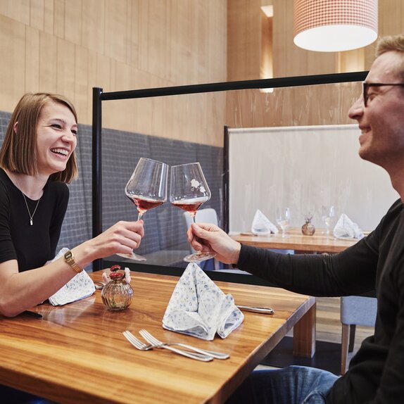 Trennwand zwischen den Tischen im Restaurant. Das Paar davor stoßt mit Wein an.