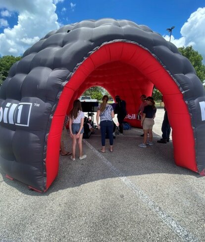 Su una piazza c'è un gonfiabile pubblicitario di Mobil 1 in rosso e nero. Sotto di esso ci sono alcune persone.